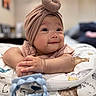 Khloe joined the competition — help win amazing prizes! baby, infant, smile, face, hands, turban_hat, cushion, toy, blue_toy, patterned_fabric, indoor, closeup, portrait, happy, child, cute, soft_light, skin, lying_down, background_blur