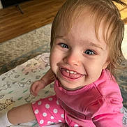 Isla is registered to the contest to win money with this photo: toddler, child, smiling, pink_clothing, polka_dots, indoor, blanket, pattern, happy, cute, face, sitting, young_child, person, expression, playful, home, floor, rug, joyful
