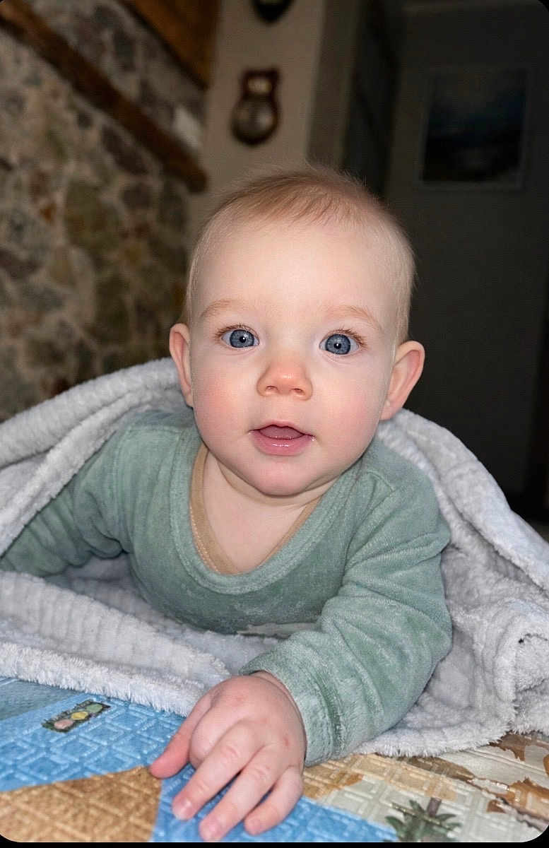 Aaron participe au concours pour gagner de l'argent avec cette photo : baby, infant, child, blue_eyes, blanket, onesie, crawling, hand, smiling, portrait, indoor, cozy, soft_texture, cheeks, gaze, looking_at_camera, bed, quilt, stone_wall, nursery