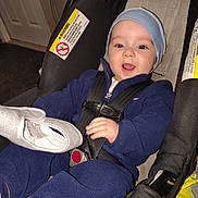 Jahari is registered to the contest to win money with this photo: baby, child, car_seat, blue_clothing, hat, smiling, indoor, seatbelt, infant, happy, person, toddler, clothing, fabric, hand, face, headwear, blanket, safety, straps