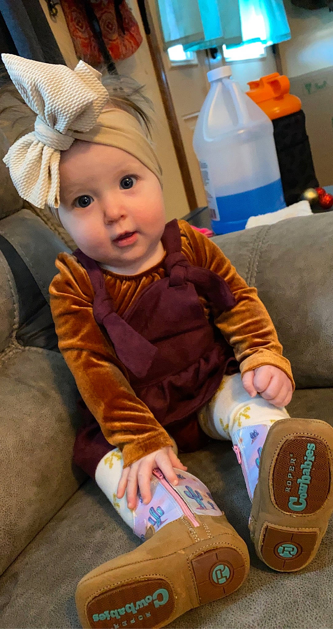 Mona is registered to the contest to win money with this photo: baby, baby_toddler_clothing, bottle, cap, cheek, child, comfort, fun, gas, happy, hat, headwear, human_leg, jacket, lap, person, plastic_bottle, room, sitting, textile