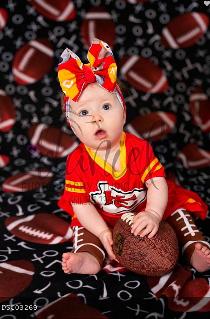 Mona is registered to the contest to win money with this photo: baby, baby_toddler_clothing, carmine, child, child_model, event, fictional_character, flash_photography, fun, grass, happy, headwear, holiday, pattern, person, portrait_photography, red, sitting, sock, surprise