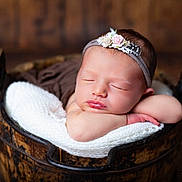 Alba a rejoint le concours — aidez-le/la à gagner de superbes lots ! newborn, baby, sleeping, headband, flower, wooden_bucket, blanket, knitted, resting, portrait, infant, peaceful, cute, soft_light, indoors, wooden_floor, closeup, child, baby_face, adorable