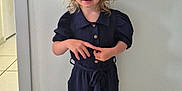 Romy participe au concours pour gagner de l'argent avec cette photo : child, toddler, hat, straw_hat, jumpsuit, navy_blue_clothing, sandals, indoor, tile_floor, standing, curly_hair, blond_hair, blue_eyes, casual_clothing, smile, person, portrait, floor, wall, buttoned_clothing