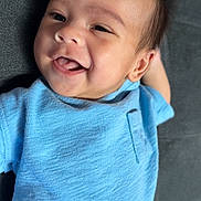Maverick is registered to the contest to win money with this photo: baby, smile, blue_shirt, infant, happy, lying_down, face, child, young, cute, skin, head, person, indoors, toddler, clothing, expression, human, portrait, one_person