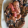 Navy is registered to the contest to win money with this photo: baby, infant, bassinet, blanket, floral_blanket, pink_cloth, hand, foot, skin, face, eyes, mouth, fingers, lying_down, wooden_floor, mesh_bassinet, cute, child, indoors, person