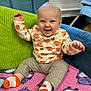 Giovanni joined the competition — help win amazing prizes! baby, child, smiling, pumpkin_print, long_sleeve_shirt, pants, socks, couch, cushion, blanket, indoor, happy, person, cute, infant, seated, playful, home, cozy, portrait