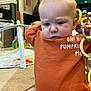 Giovanni is registered to the contest to win money with this photo: baby, child, indoor, orange_sweater, toy, plastic_chain, carpet, play_gym, curious, sitting, infant, person, furniture, home, face, head, clothing, expression, floor, room
