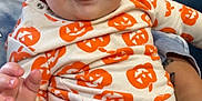 Giovanni is registered to the contest to win money with this photo: baby, child, infant, tongue, smile, pumpkin_pattern, clothing, person, indoor, furniture, crib, tattoo, hand, face, cute, happy, seated, adult, holding, blue_eyes