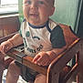 Giovanni joined the competition — help win amazing prizes! baby, child, high_chair, wooden_chair, shirt, text_on_shirt, happy, smiling, indoor, window, sunlight, green_wall, floor_tiles, person, cute, infant, chubby_cheeks, seated, hands, legs