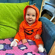 Giovanni joined the competition — help win amazing prizes! baby, child, orange_hoodie, pumpkin_costume, smiling, blue_chair, green_cushion, pink_blanket, purple_hippos, indoors, cute, happy, sitting, cozy, infant, person, footwear, white_socks, playful, portrait