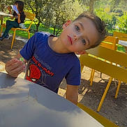 Thays participe au concours pour gagner de l'argent avec cette photo : child, boy, girl, outdoor, park, table, chair, yellow_chair, blue_shirt, spiderman_shirt, food, reading, trees, sunlight, daylight, greenery, playing, curious, casual_clothing, relaxing