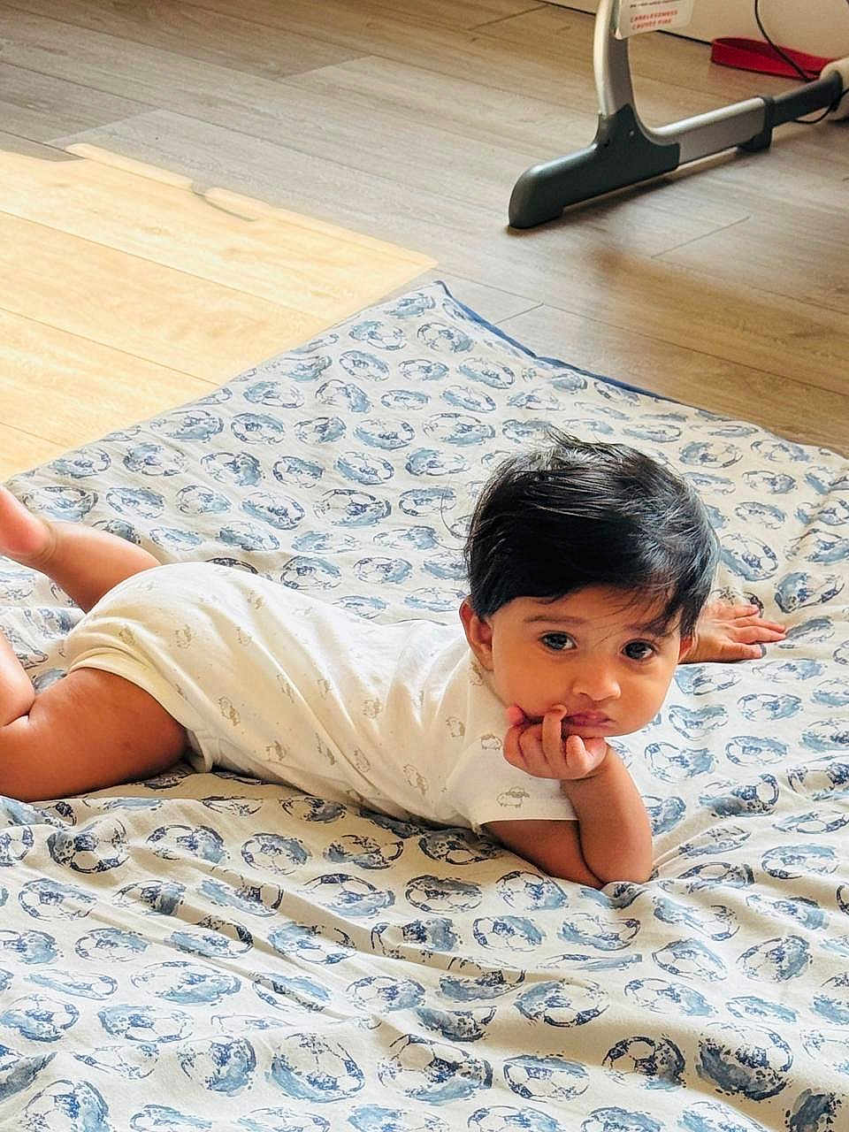 Cristiano joined the competition — help win amazing prizes! baby, child, infant, blanket, floor, wooden_floor, indoors, person, cute, resting, hand_on_chin, contemplative, patterned_blanket, exercise_equipment, home, young_child, lying_down, casual_clothing, short_sleeves, black_hair