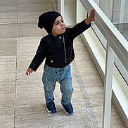 George joined the competition — help win amazing prizes! toddler, child, indoor, black_jacket, beanie, jeans, sneakers, walking, railing, curious, floor, window, glass, exploring, person, young_child, fashion, casual, daylight, portrait