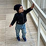 toddler, child, indoor, black_jacket, beanie, jeans, sneakers, walking, railing, curious, floor, window, glass, exploring, person, young_child, fashion, casual, daylight, portrait