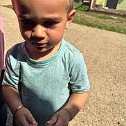 George is registered to the contest to win money with this photo: child, toddler, outdoor, sunlight, curious, holding_object, short_hair, blue_shirt, shadow, grass, building, daylight, person, young_child, casual_clothing, nature, portrait, closeup, standing, summer