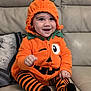 George is registered to the contest to win money with this photo: baby, child, pumpkin_costume, orange_hoodie, striped_socks, smiling, happy, cute, indoors, couch, seated, costume, hood, fall, festive, portrait, person, holiday, cozy, cute_outfit