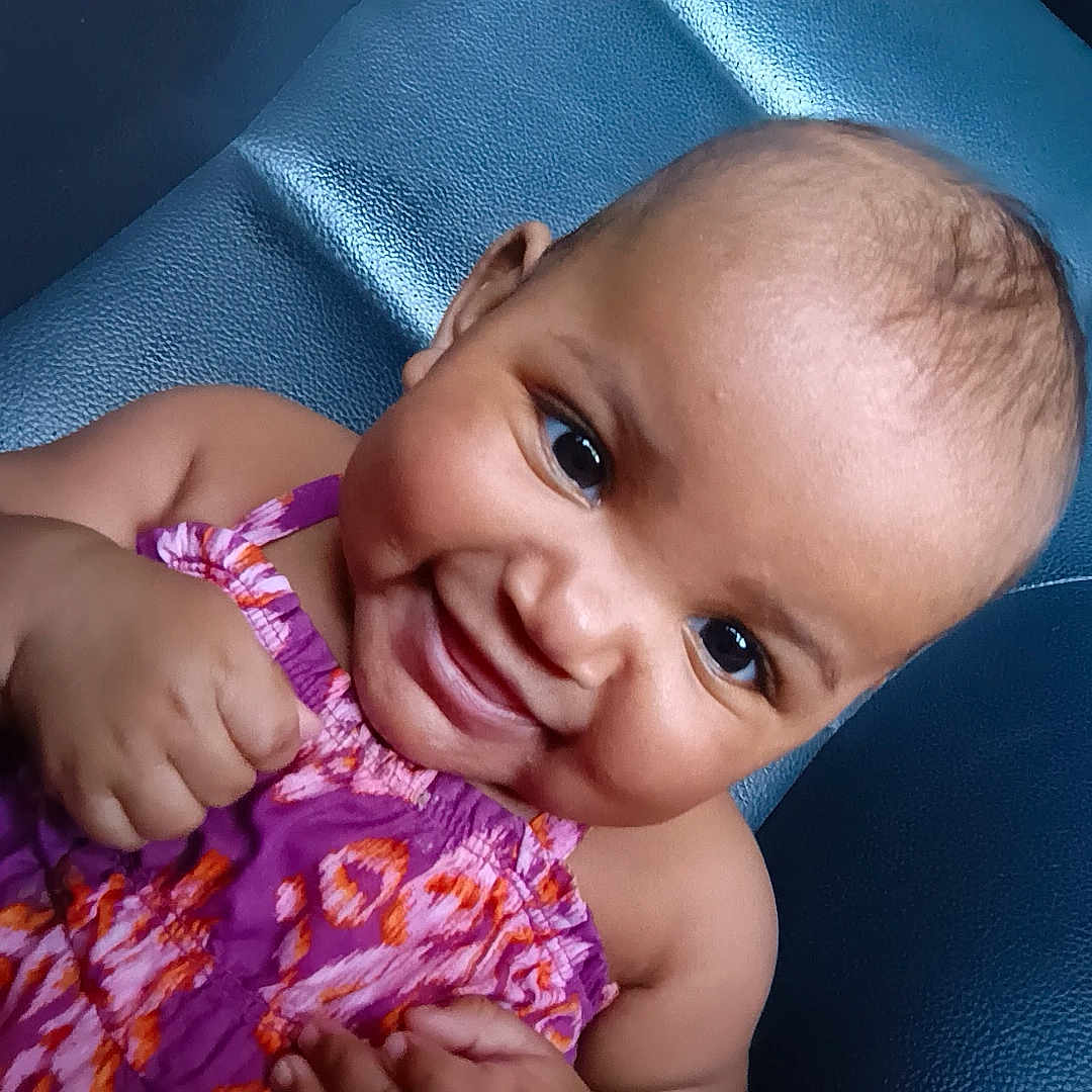 Mileyah joined the competition — help win amazing prizes! arm, baby, child, closeup, cute, face, hand, happy, indoors, infant, leather, patterned_clothing, person, portrait, purple_dress, seat, sitting, skin, smiling, young_child