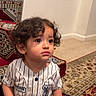 Dawud joined the competition — help win amazing prizes! baseball_outfit, carpet, casual, child, clothing, curly_hair, cute, expression, floor, indoor, looking_away, patterned_carpet, person, portrait, sitting, stairs, striped_clothing, toddler, wall, young_child