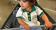 Dawud is registered to the contest to win money with this photo: blue_shorts, casual_clothing, child, clothing_store, curious, curly_hair, footwearless, green_trim, holding, indoor, person, polo_shirt, portrait, retail, shopping, shopping_cart, store_aisle, toddler, white_cap, young_child