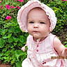 baby, child, pink_bonnet, pink_dress, flowers, greenery, plants, outdoor, nature, garden, cute, portrait, infant, face, headwear, summer, sunlight, young_child, skin, expression