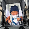 baby, stroller, hat, knit_hat, child, infant, seat_belt, outdoor, clothing, striped_shirt, jacket, face, person, hands, headwear, safety, baby_bib, wheel, transport, cute