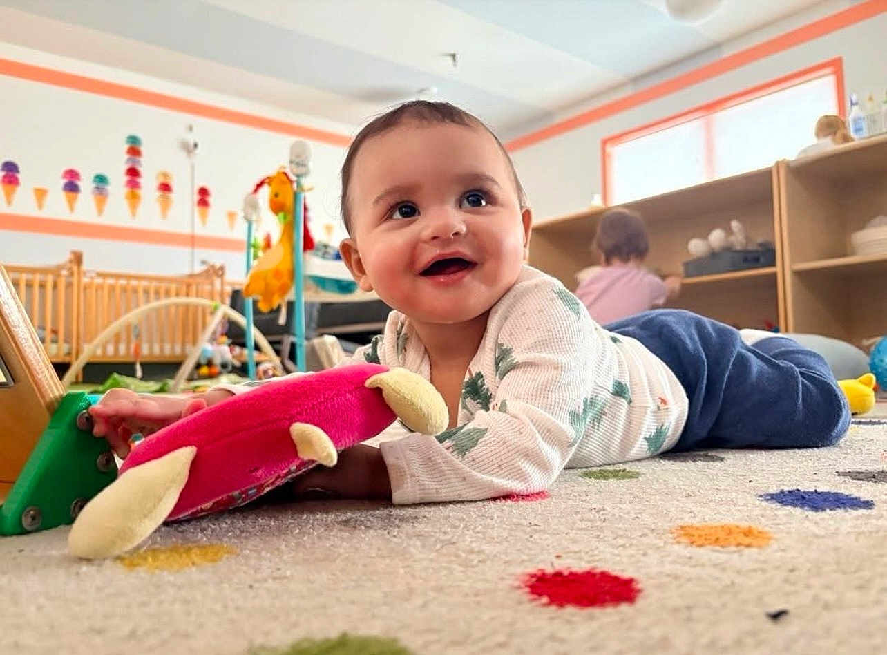 Nevaeh is registered to the contest to win money with this photo: baby, child, toy, plush_toy, carpet, colorful, nursery, crib, furniture, smiling, indoor, playroom, person, crawling, happy, floor, clothing, sleepshirt, pants, toddler