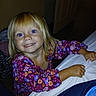 child, girl, blonde_hair, smile, red_eye, floral_dress, purple_clothing, indoor, bed, hand, face, happy, cute, portrait, person, young_child, grip, fabric, room, playful