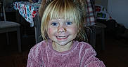 Jade is registered to the contest to win money with this photo: child, smiling, blonde_hair, pony_tail, pink_sweater, indoor, living_room, table, chair, water_bottle, plaid_jacket, wooden_floor, happy, person, casual_clothing, face, portrait, messy_hair, cozy, home