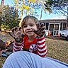 Charlee is registered to the contest to win money with this photo: child, muddy_hands, smile, outdoor, trees, fire_pit, house, grass, red_shirt, striped_sleeves, daylight, playful, person, nature, car, orange_cones, background, happy, young_child, casual_clothing