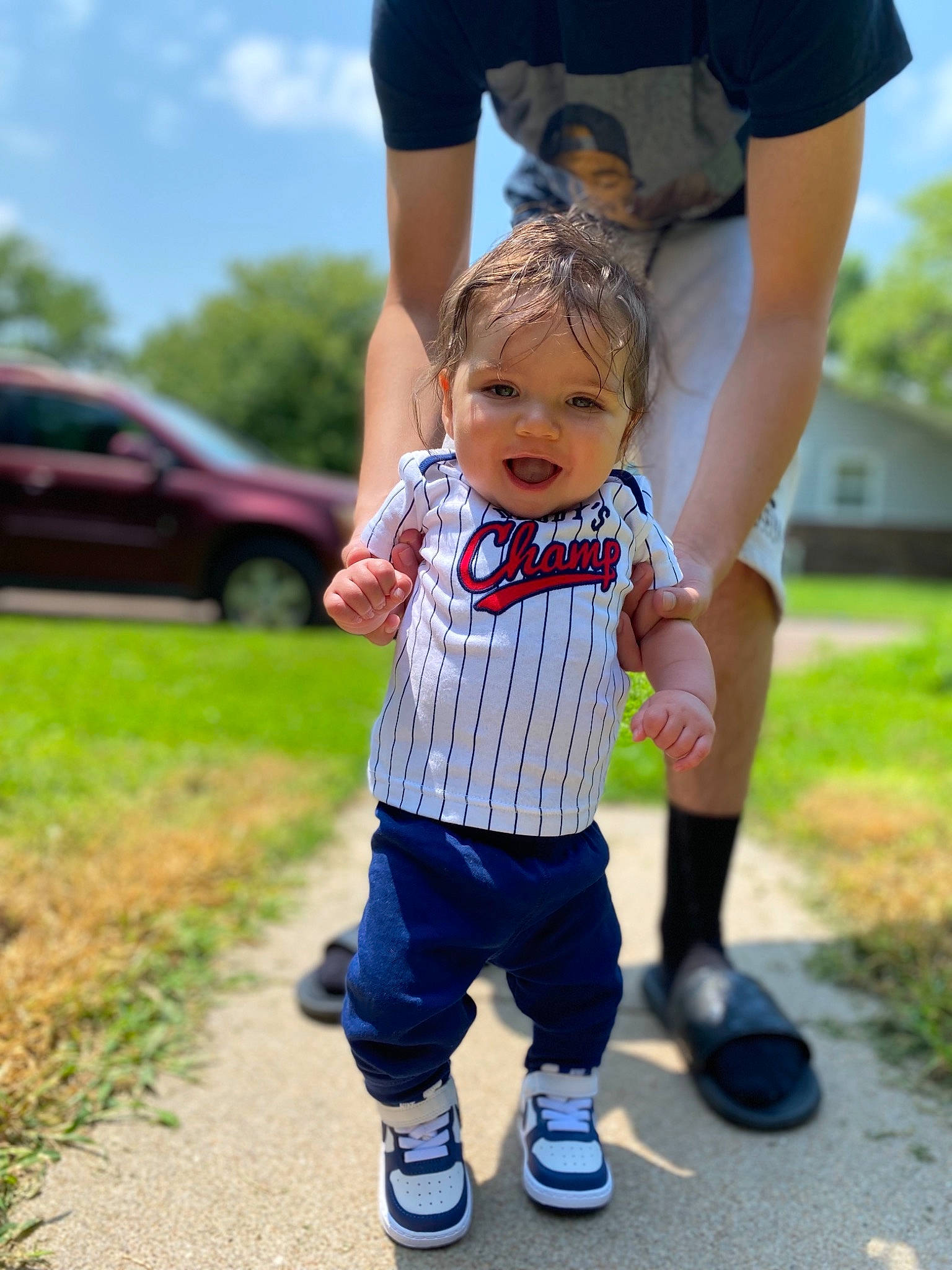 Kobi is registered to the contest to win money with this photo: blue, footwear, gesture, grass, hand, happy, leg, leisure, people, people_in_nature, person, plant, recreation, shoe, sky, smile, sneakers, style, toddler, tree