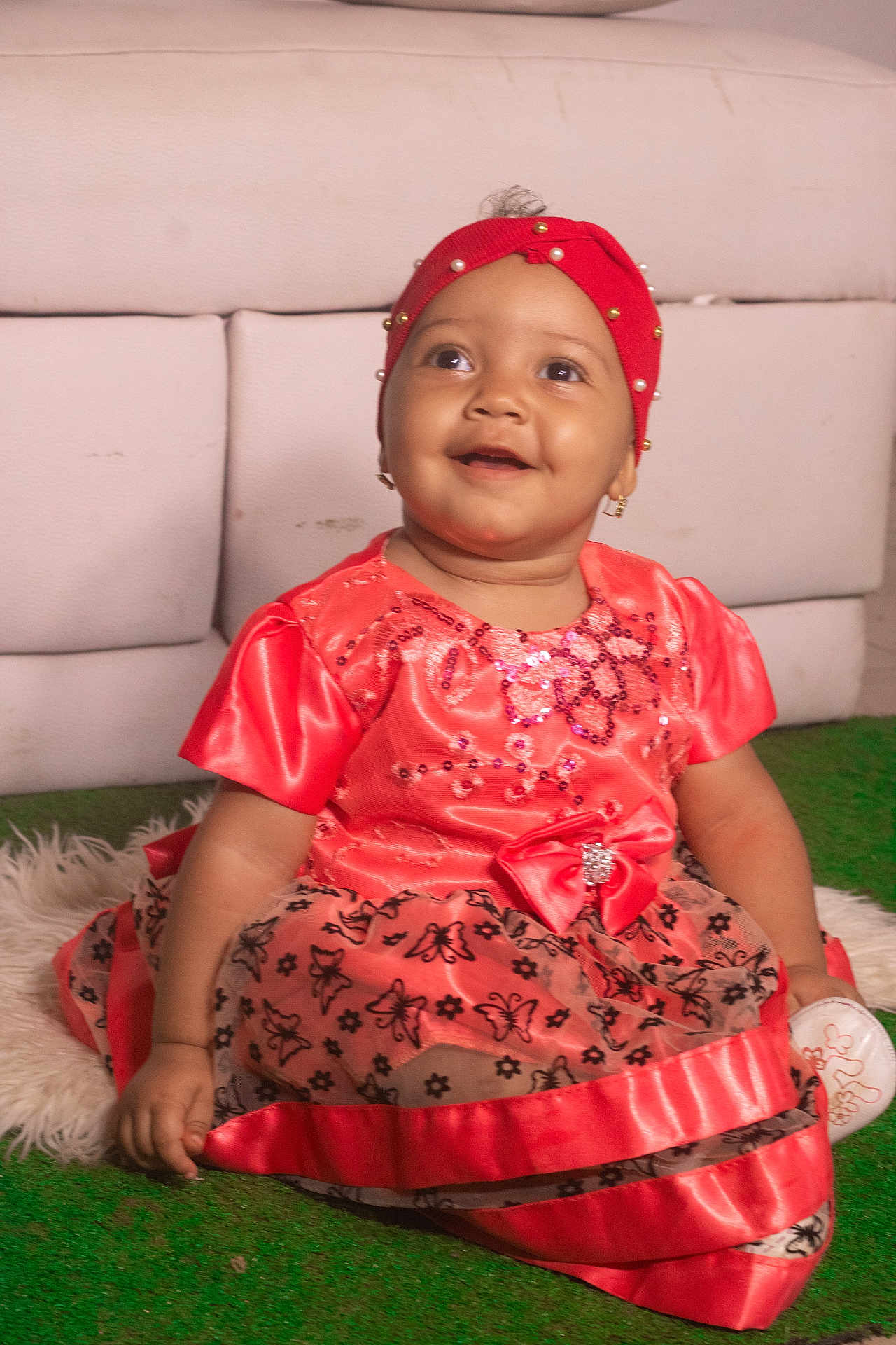 Ioana is registered to the contest to win money with this photo: baby, child, smiling, dress, coral_color, headband, pearl, sitting, carpet, green, white_rug, indoor, portrait, cute, happy, earring, pattern, butterfly, sparkle, fabric