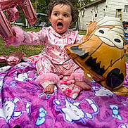 Eleftheria is registered to the contest to win money with this photo: toddler, child, balloon, pink_pajamas, blanket, hello_kitty, outdoor, grass, backyard, house, fence, toy, curly_hair, expression, sitting, playful, colorful, foot, person, celebration