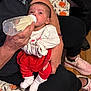 Chloee is registered to the contest to win money with this photo: baby, bottle, feeding, adult_hand, red_clothing, white_sock, blanket, floor, sneakers, person, indoor, cute, infant, holding, toddler, sitting, casual, home, cozy, portrait