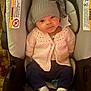 baby, infant, child, car_seat, hat, knitted_sweater, pink_clothing, gray_hat, star, white_socks, blue_pants, indoors, cute, young_child, seated, car_seat_warning_label, portrait, cozy, warm_clothing, looking_at_camera