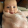 baby, blanket, pink, face, infant, cute, wrapped, cozy, indoor, portrait, expression, soft_texture, child, person, newborn, carpet, dresser, wooden_furniture, warm, smile