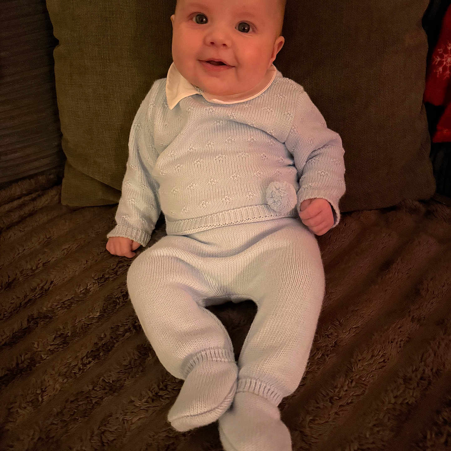 Reggie joined the competition — help win amazing prizes! baby, blanket, blue_clothing, child, comfort, cozy, cute, face, happy, home, indoors, infant, knitwear, person, pillow, portrait, sitting, smile, soft_texture, warm