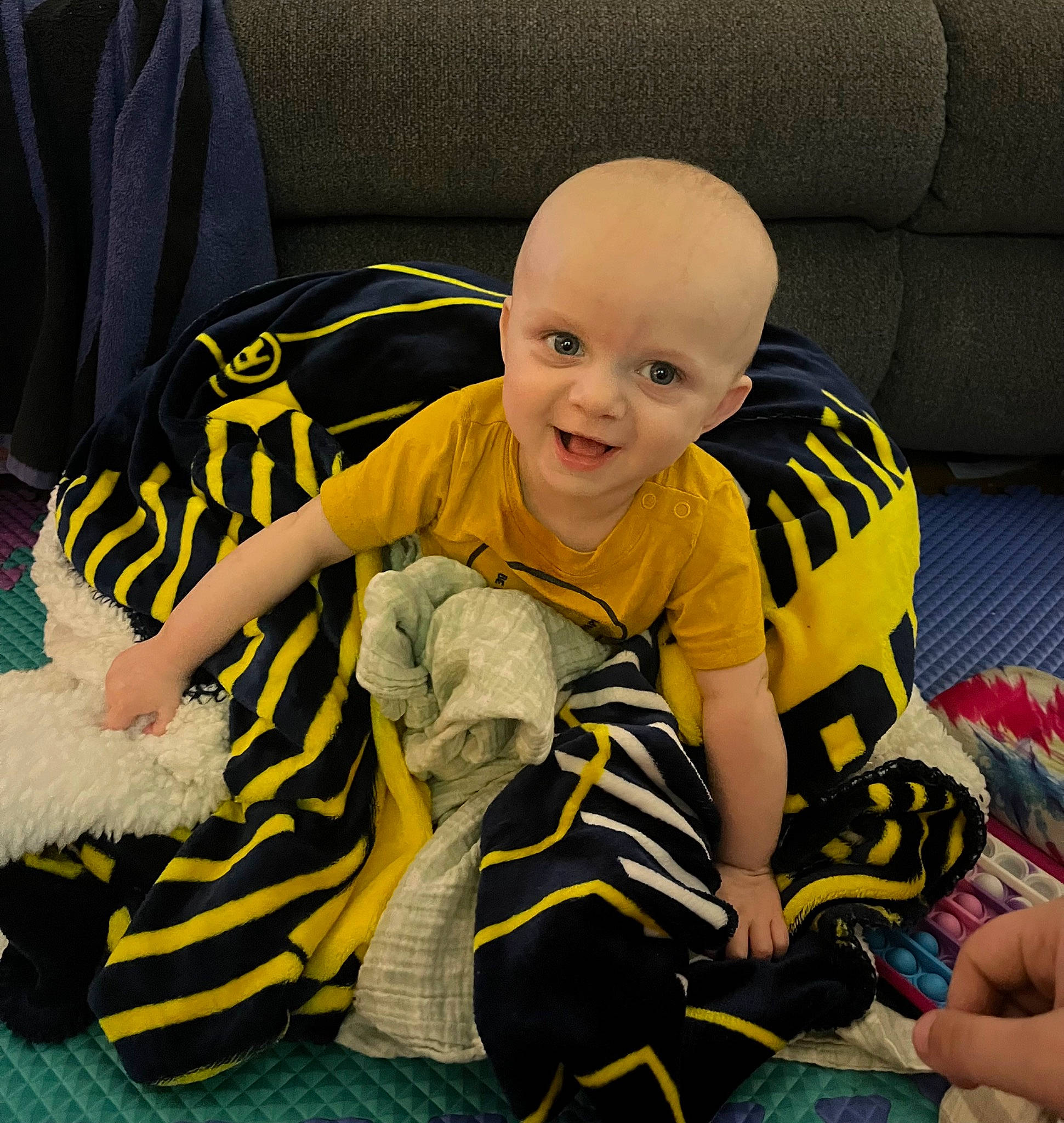 Declan is registered to the contest to win money with this photo: baby, baby_toddler_clothing, black, child, comfort, flooring, fun, happy, joy, lap, leg, person, product, shoe, sitting, sleeve, smile, sneakers, sock, toddler