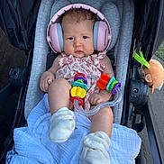 Astrid is registered to the contest to win money with this photo: baby, child, headphones, stroller, toy, colorful, pink, boots, blanket, infant, cute, outdoor, person, clothing, seat, accessory, play, young, portrait, babywear