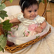 Mayra joined the competition — help win amazing prizes! baby, child, wicker_basket, white_dress, pink_flowers, headband, flower, leaf, greenery, indoor, floor, wooden_floor, cute, smile, portrait, infant, adorable, sitting, bracelet, decorative