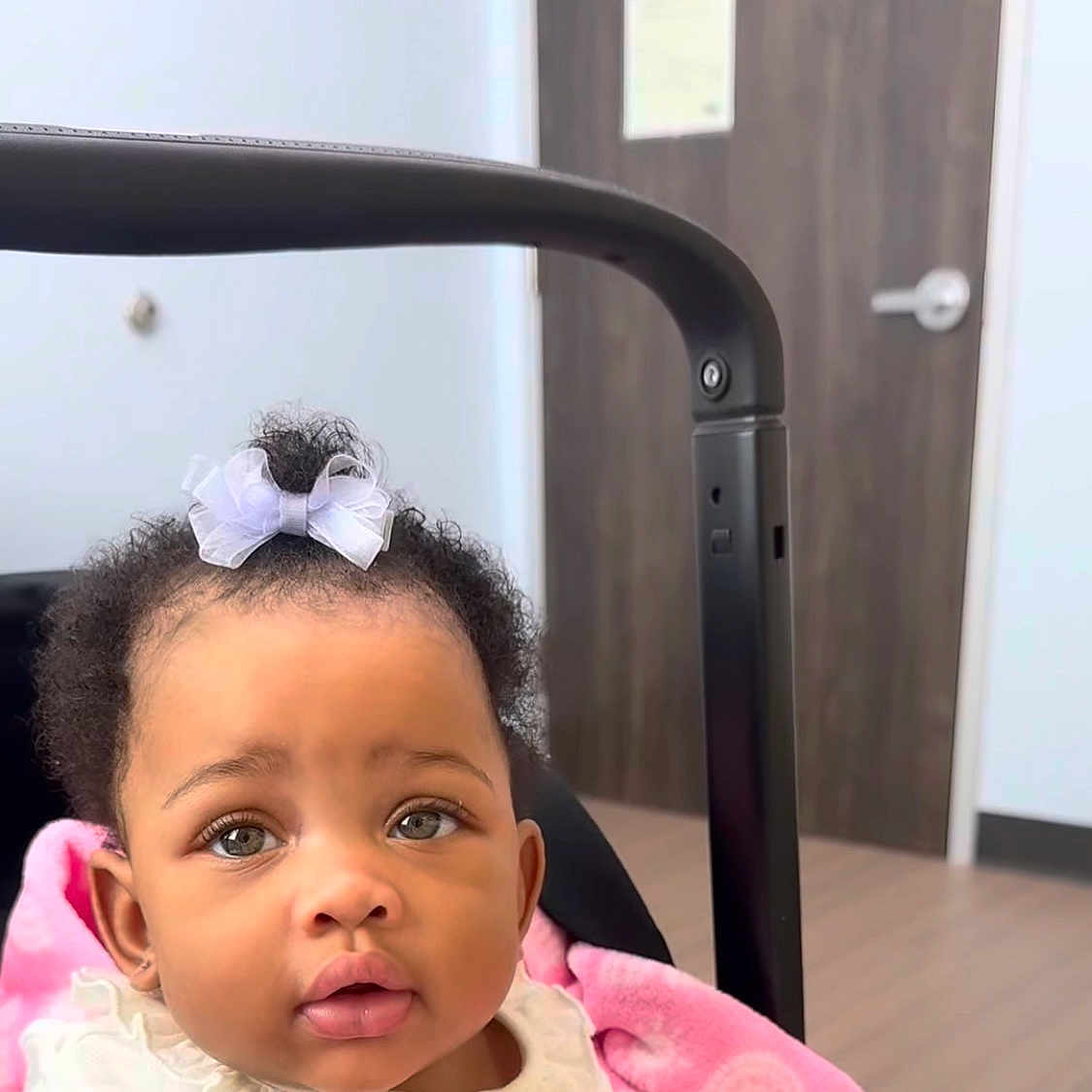 Kenzlii joined the competition — help win amazing prizes! adorable, baby, bow, child, clothing, curly_hair, cute, door, expression, eyes, face, head, indoor, infant, mouth, person, pink_blanket, portrait, stroller, wooden_door