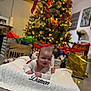 baby, blanket, christmas_tree, gifts, holiday, festive, smiling, indoors, floor, decorations, lights, red_ribbon, cozy, happy, child, person, home, celebration, wrapped_presents, knitted