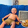 Oden joined the competition — help win amazing prizes! baby, child, boy, donut, food, plate, sign, blue_blanket, shorts, smile, milestone, celebration, indoor, window, curtain, face, skin, hand, foot, happy