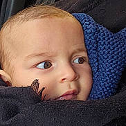 Alf a rejoint le concours — aidez-le/la à gagner de superbes lots ! baby, infant, face, eyes, close_up, knit_scarf, blanket, car_interior, car_window, seat, portrait, brown_eyes, head, cheek, cozy, wrapped, clothing, looking_away, outdoor_background, red_building
