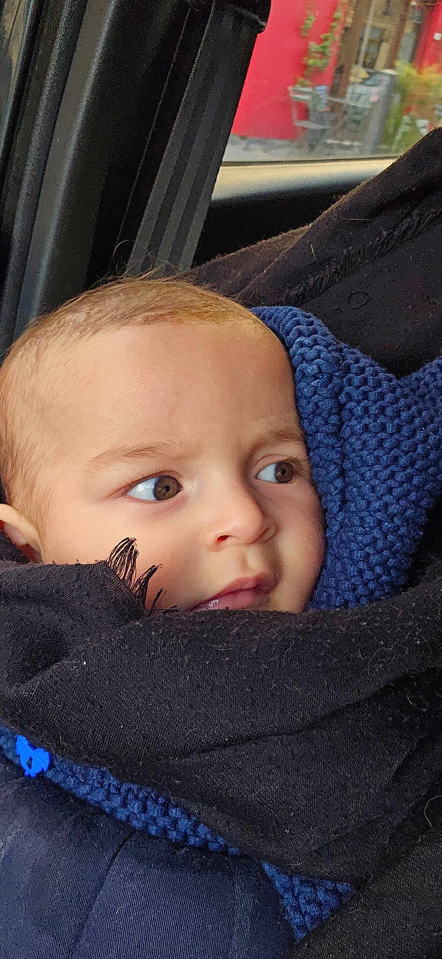 Alf a rejoint le concours — aidez-le/la à gagner de superbes lots ! baby, infant, face, eyes, close_up, knit_scarf, blanket, car_interior, car_window, seat, portrait, brown_eyes, head, cheek, cozy, wrapped, clothing, looking_away, outdoor_background, red_building