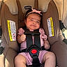 baby, car_seat, child, infant, pink_bow, pink_outfit, pacifier, sunlight, canopy, seatbelt, straps, brown_car_seat, warning_labels, cute, expression, indoors, person, comfortable, sitting, headband