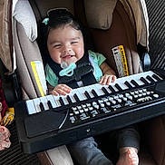 Valentina is registered to the contest to win money with this photo: baby, car_seat, child, clothing, cushion, feet, footwear, hands, happy, indoor, infant, keyboard, music, pacifier, plush_toy, portrait, seat_belt, small_keyboard, smiling, toy