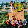 balloon, buzz_lightyear, cardboard_box, child, daylight, grass, horse, mr_potato_head, mrs_potato_head, number_2, outdoor, park, piggy_bank, rex, slinky_dog, smiling, toddler, toy_story, toys, woody