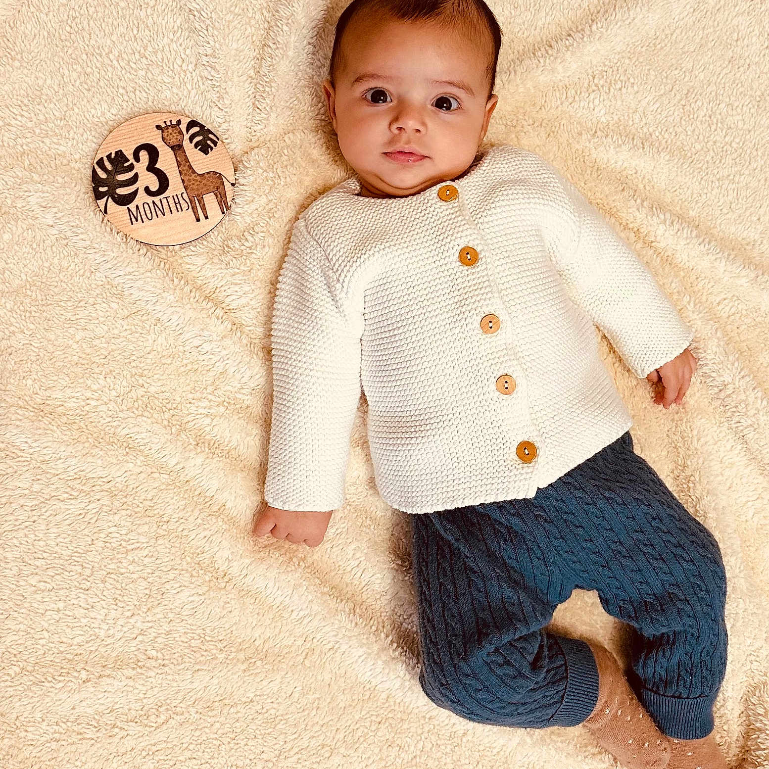 Lorenzo a rejoint le concours — aidez-le/la à gagner de superbes lots ! baby, blanket, blue_pants, child, cozy, curious_expression, cute, giraffe, indoors, infant, knitwear, lying_down, months_marker, portrait, small_hands, socks, soft_texture, warm_colors, white_sweater, wooden_sign