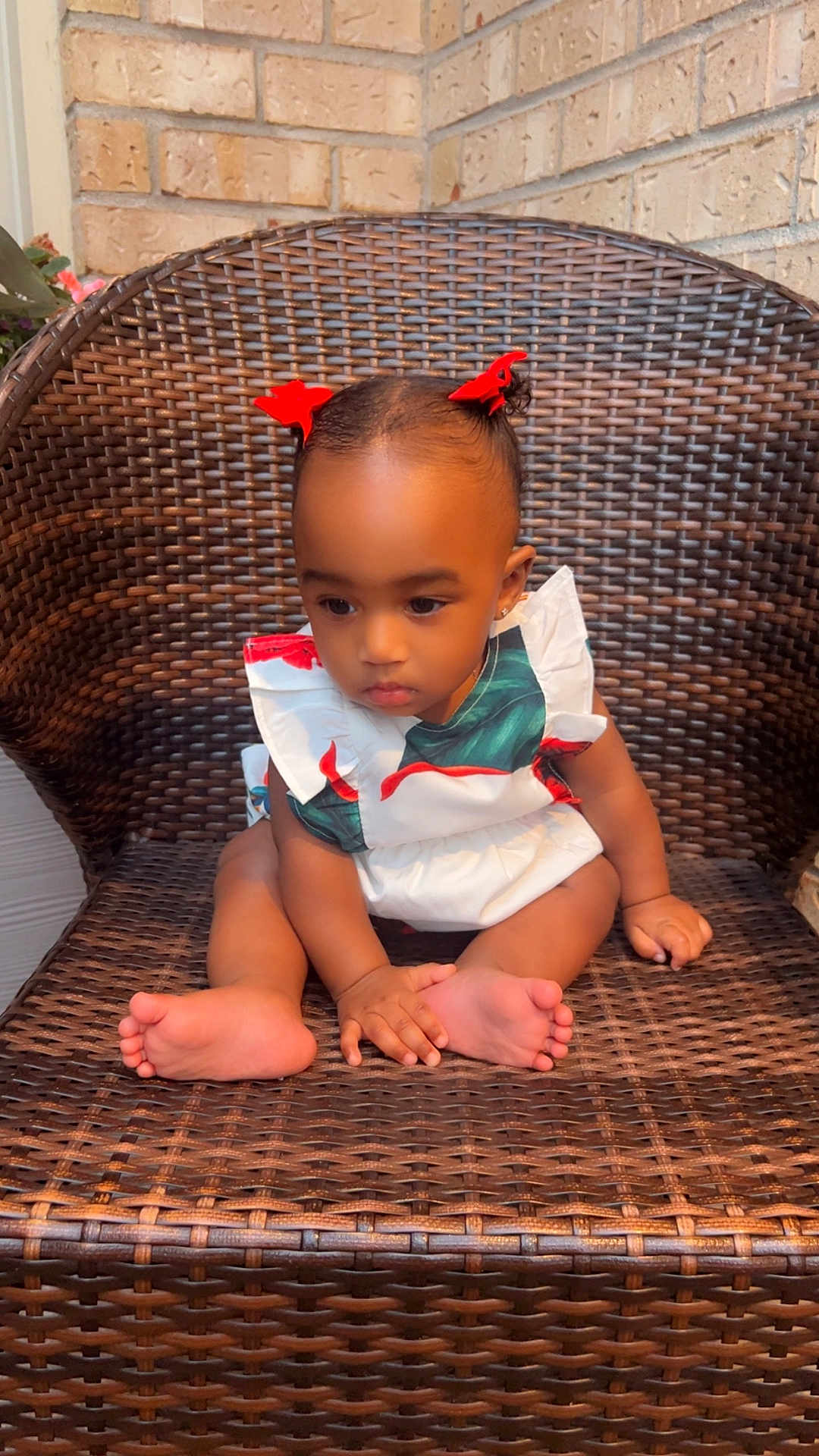Brielle is registered to the contest to win money with this photo: toddler, child, baby, sitting, wicker_chair, red_bows, hair_accessories, barefoot, hands, feet, white_dress, patterned_clothing, brick_wall, outdoor, portrait, cute, young_child, person, expression, furniture